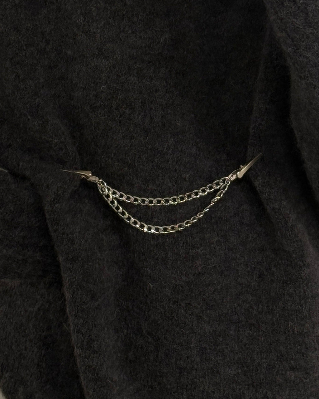 Person wearing a dark gray sweater with a chain clothing clip on a neutral background