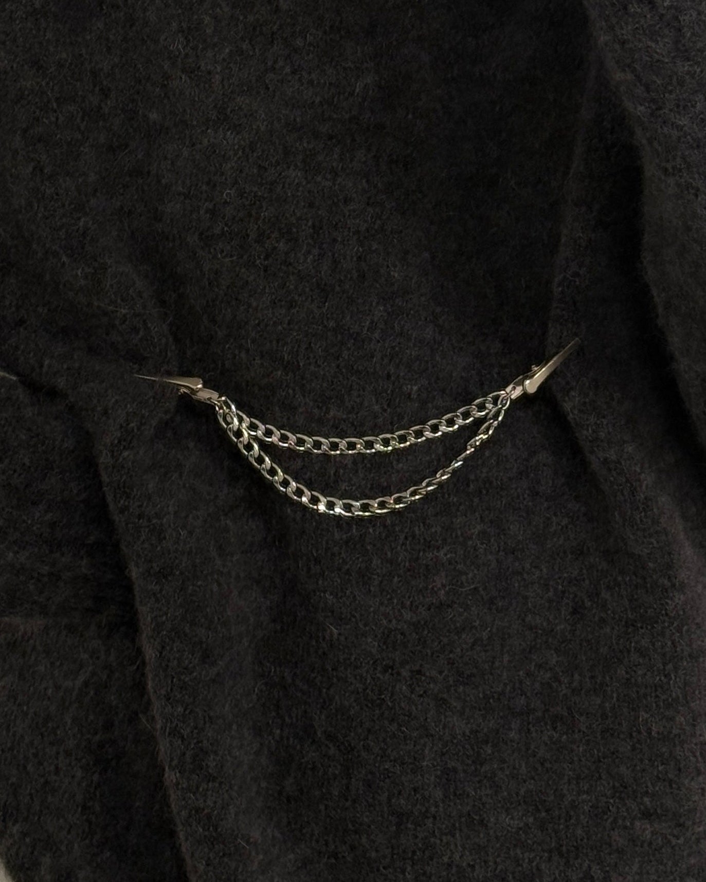 Person wearing a dark gray sweater with a chain clothing clip on a neutral background
